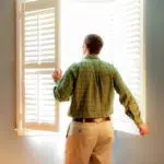 A man opening some window shades.