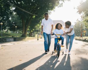 Family playing in park teaching daughter to ride a bike